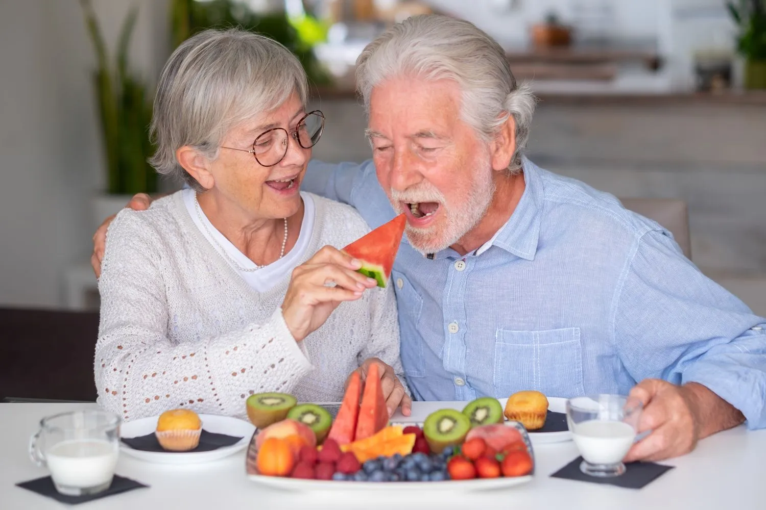 Senior woman feeding senior man soft food (watermelon) at home