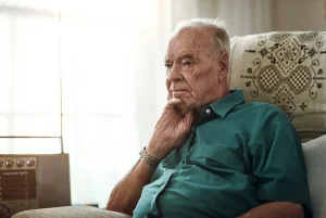 Senior man with Alzheimer’s sitting thoughtfully on couch