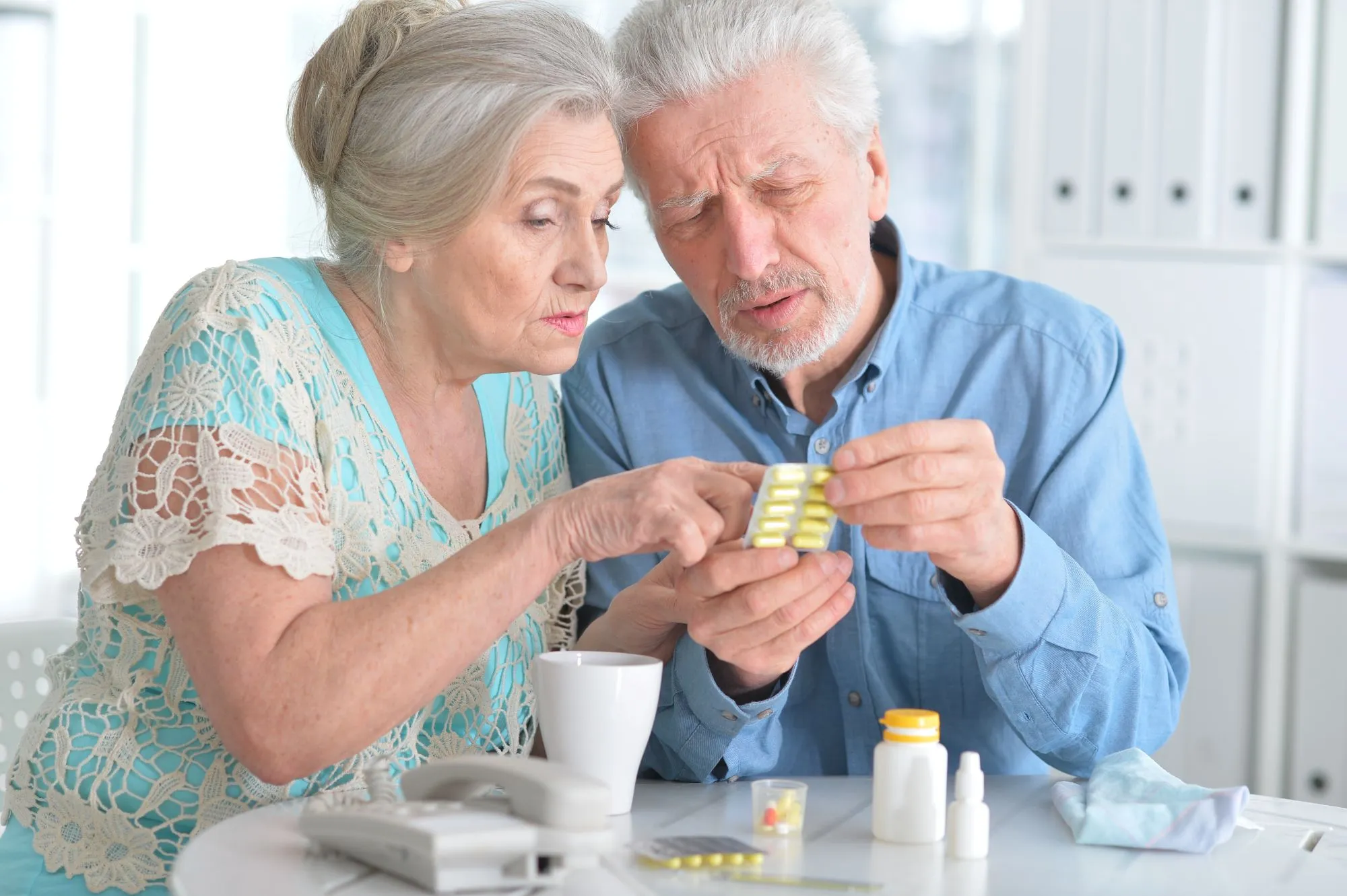 elderly couple looking closely at a blister pack of vitamin supplements while sitting at a table