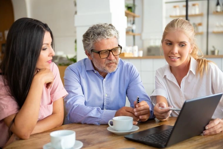 Colleagues discuss retirement planning while looking at a laptop in a cafe
