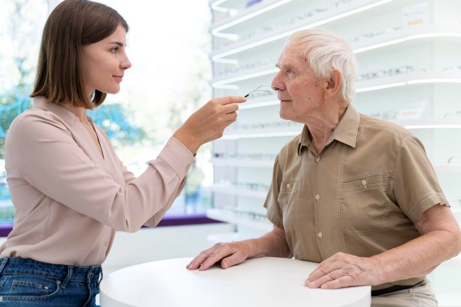 Young lady helping senior man try glasses