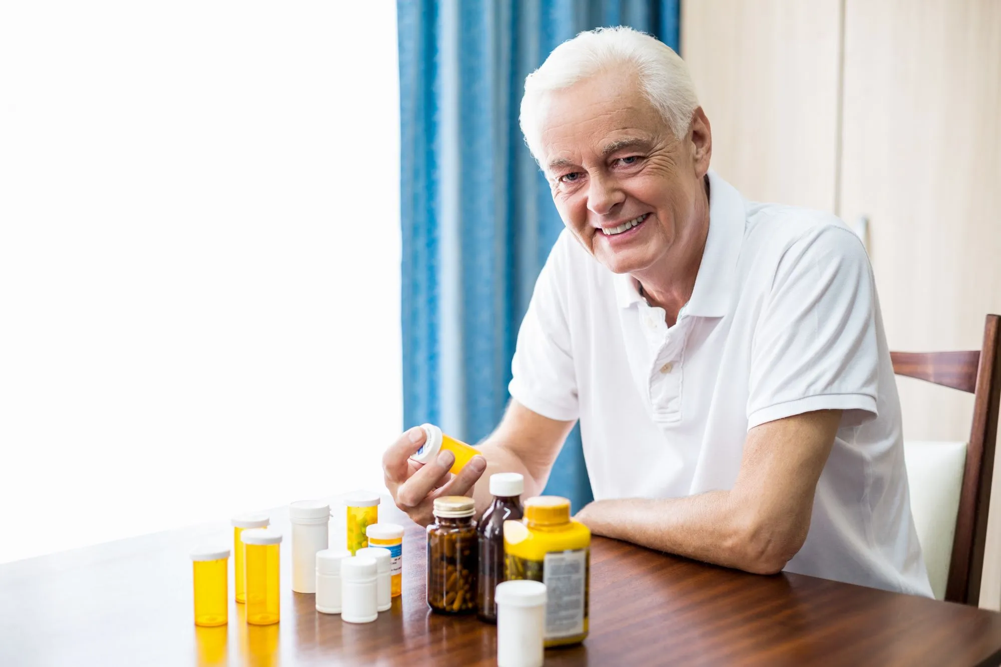 smiling senior man sitting at a table with various vitamin supplements