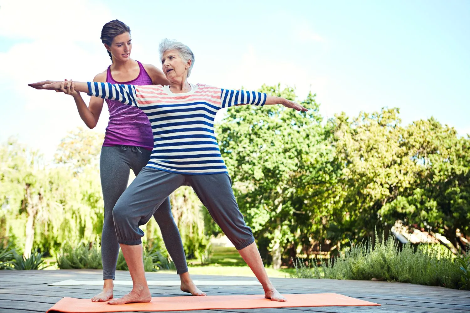 Senior woman practicing yoga outdoors with instructor after exercise.