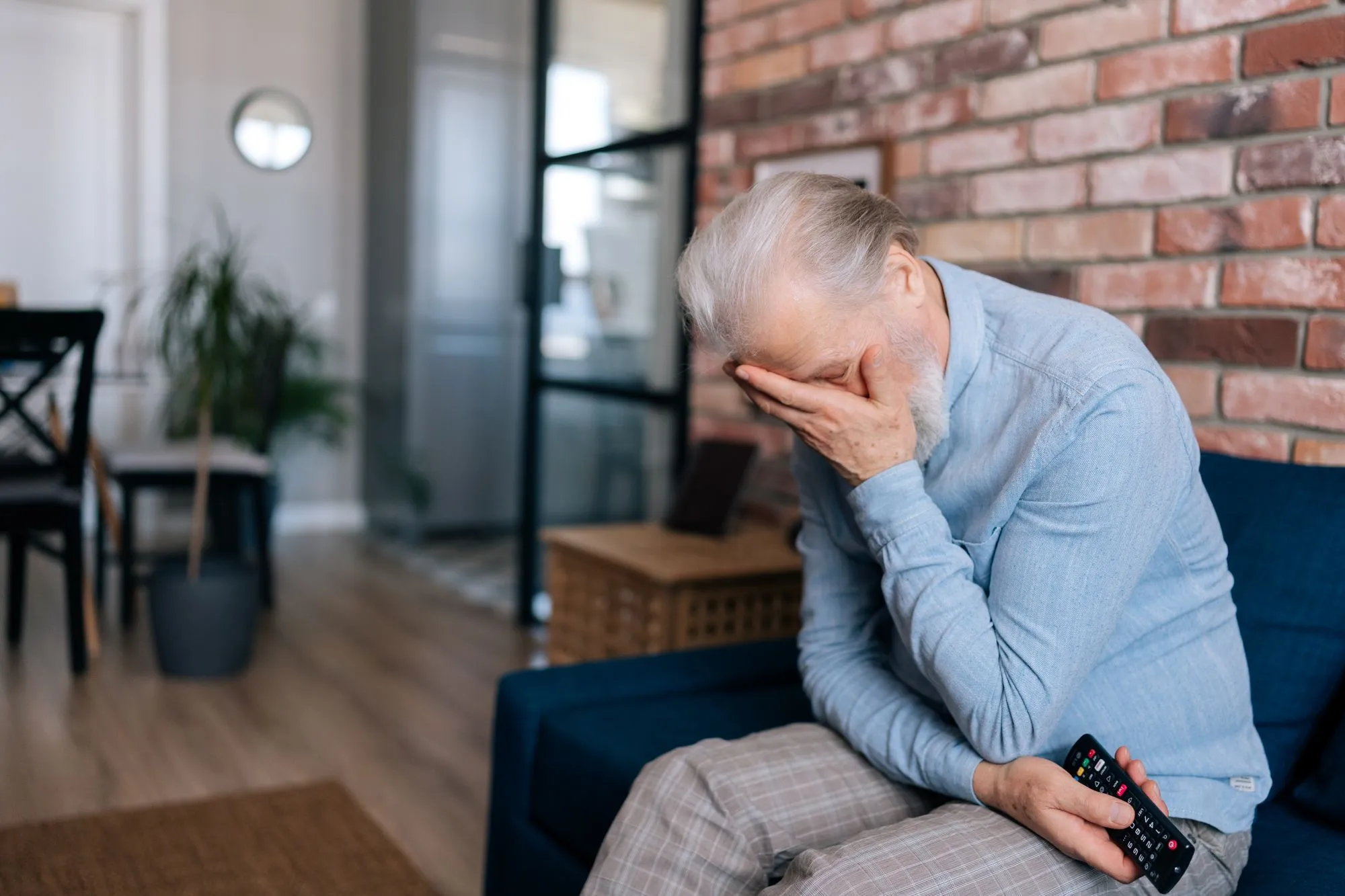 White-haired senior man sitting worried on sofa at home